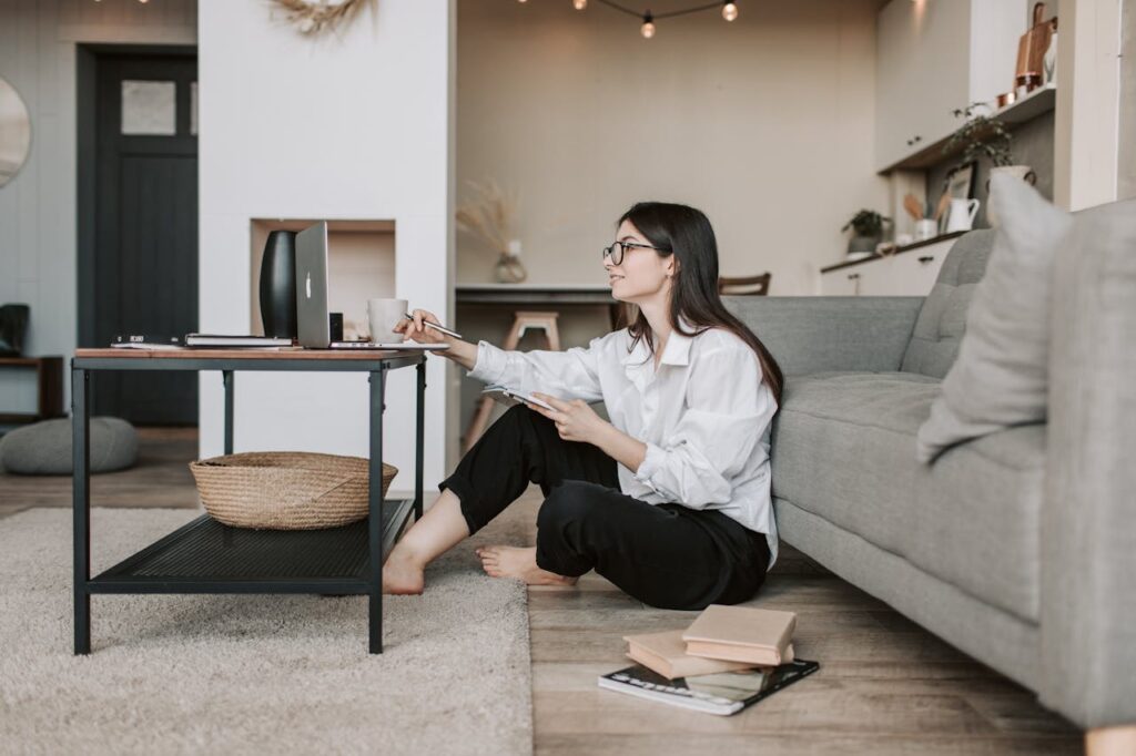 Woman using a laptop while sitting on the floor of a cozy living room, epitomizing work-from-home lifestyle.